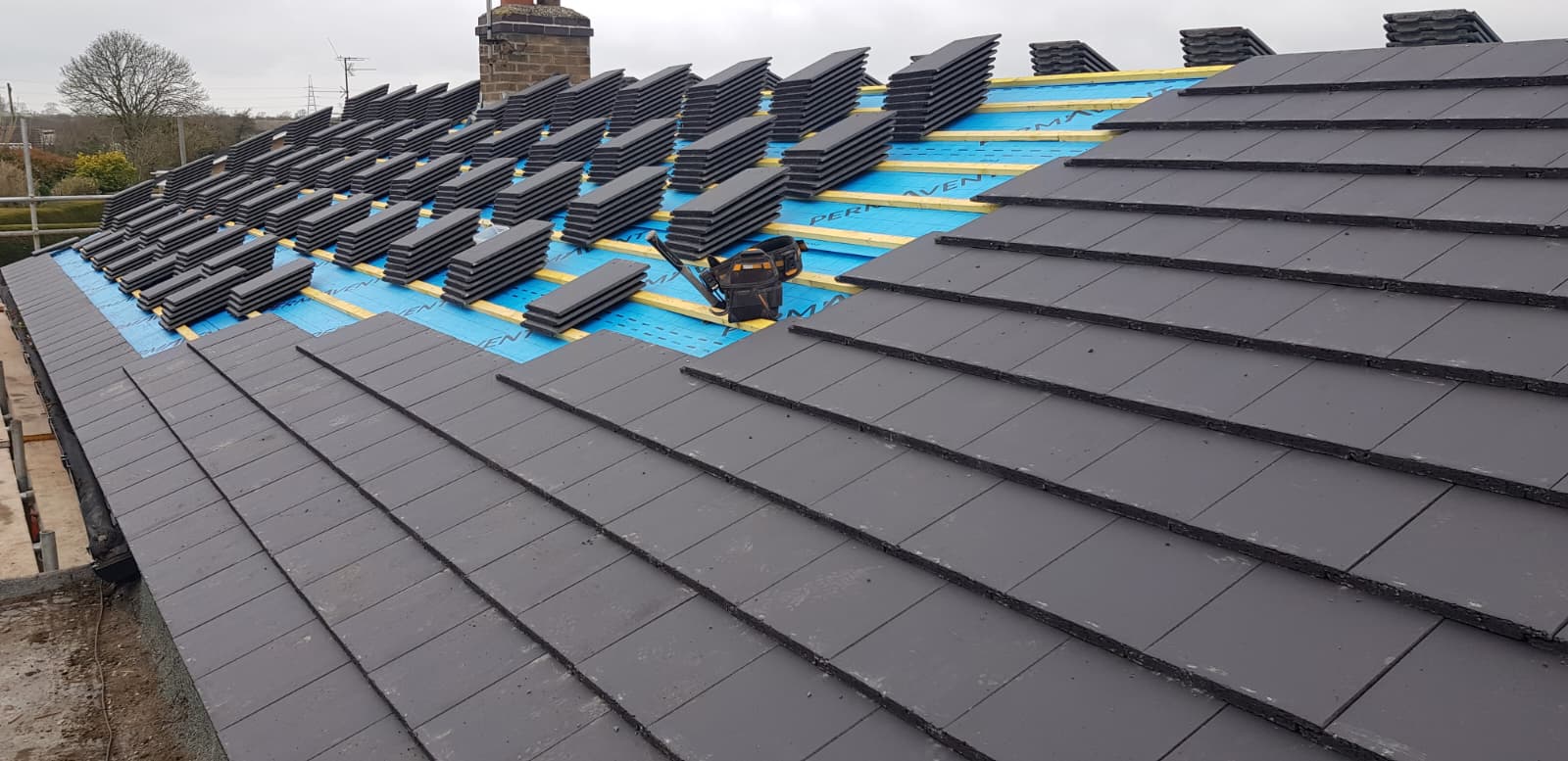 Roofing team stripping a scaffolded bungalow roof with work vans on site