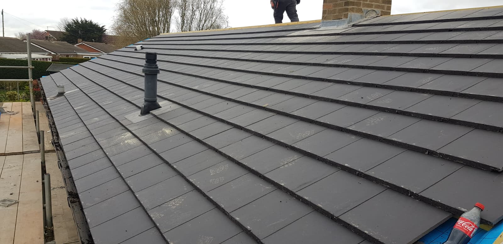 Close-up of newly laid grey tiled roof with roofer working at the edge