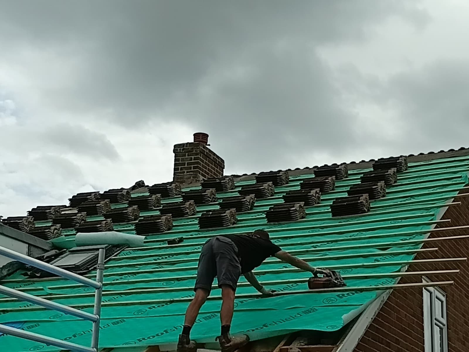 Detached house with mobile tower scaffold and roofer carrying out roof repairs