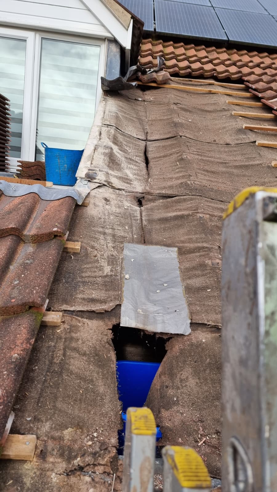 Damaged old felt with temporary patch and hole exposing loft space before re-roof